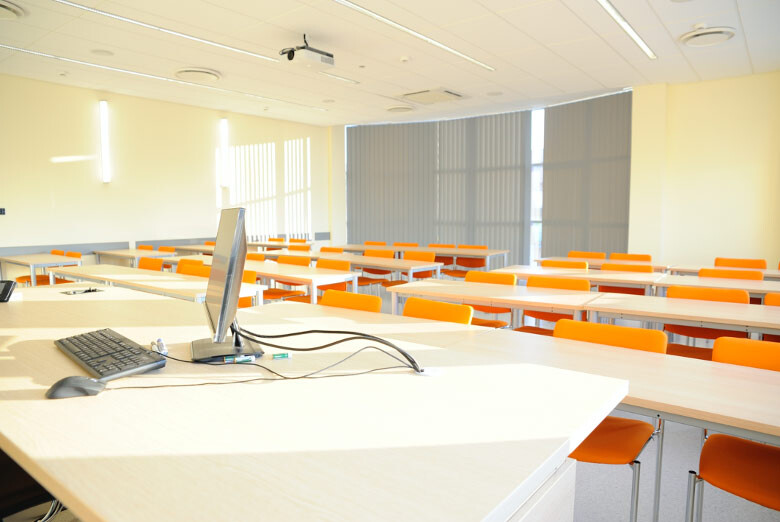 Sala A220 - widok zza stanowiska komputerowego prowadzącego na stoły i pomarańczowe krzesła.