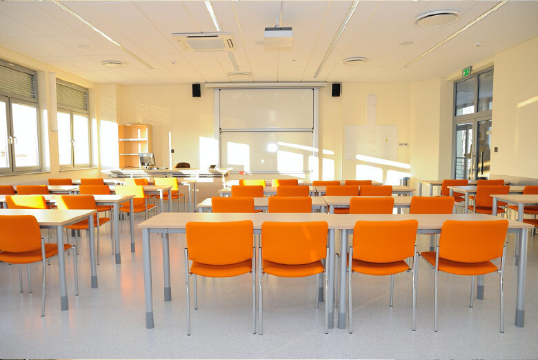 Sala A220 - rzędy stołów i krzeseł skierowane w stronę tablicy oraz ekranu projekcyjnego.