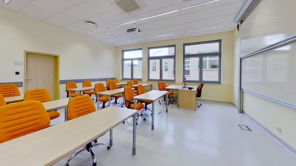 Sala A217 - stoły z pomarańczowymi krzesłami obrotowymi, biurko prowadzącego i tablica.