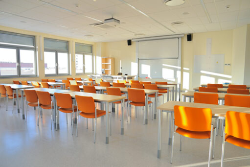 Sala A325 - stoły w układzie szkolnym, pomarańczowe krzesła i ekran nad tablicą.