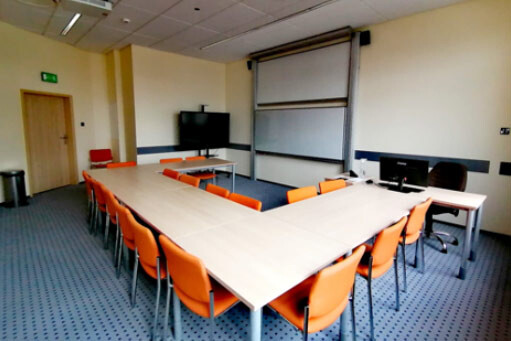 Sala A309 - stoły ustawione w podkowę, ekran projekcyjny i stanowisko komputerowe prowadzącego.