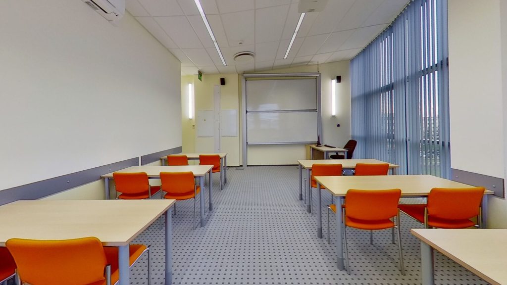 Sala A310 - dwa ciągi stołów z przejściem pośrodku, tablica i ekran projekcyjny.