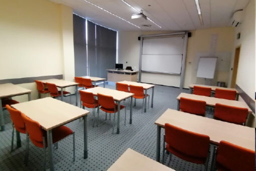 Sala A311 - stoły i pomarańczowe krzesła w układzie szkolnym, tablica oraz flipchart.