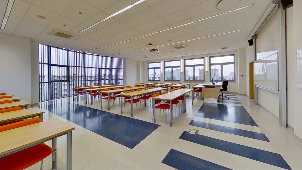 Sala A423 - widok ogólny na rzędy stołów, duże okna i biurko prowadzącego przy tablicy.