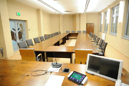 Sala 404 - stanowisko z monitorem i mikrofonem na tle stołów konferencyjnych w podkowę.