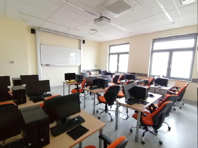 Pracownia A403 - rzędy stanowisk komputerowych skierowane w stronę tablicy i ekranu.